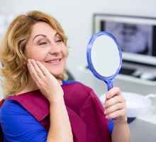 Older patient examining her smile with a mirror
