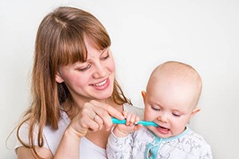 Mother helping baby brush teeth