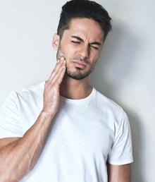 Man with dental pain placing a hand on his cheek.